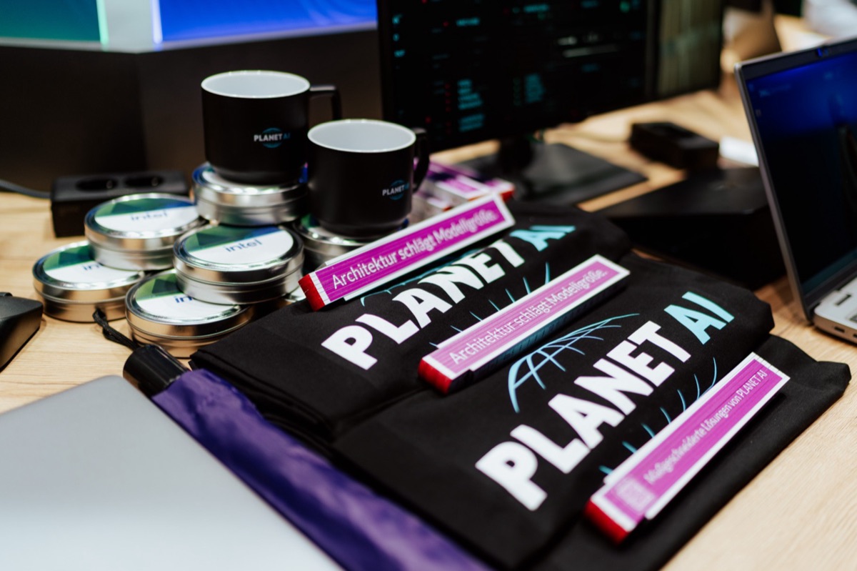 PLANET AI shirts, mugs and folding rulers reading “Architektur schlägt Modellgröße” at the stand