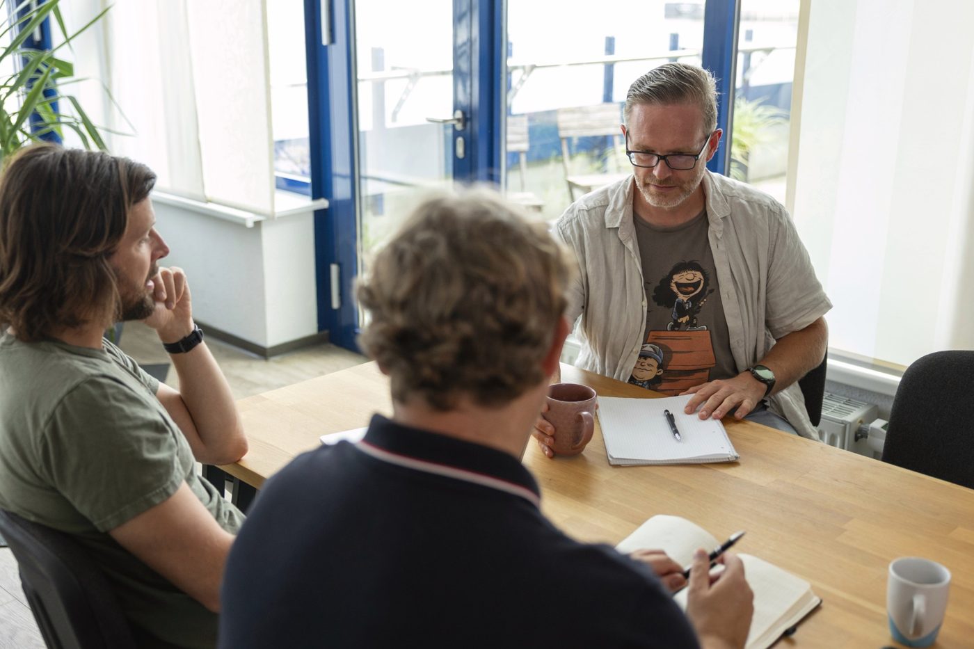 Three colleagues talking at a table with notebooks and coffee cups